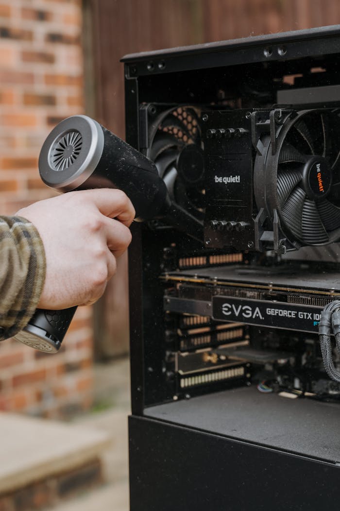 About Person cleaning desktop computer components with an electric duster outside.